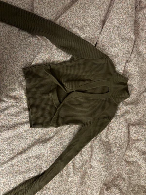 Olivgrön ribbad polotröja från Zara - Säljer en olivgrön ribbad polotröja från Zara med snygg omlott-detalj framtill och hög krage. Tröjan har lång ärm och är tillverkad i mjukt stickat material som sitter skönt på kroppen. Perfekt för dig som gillar trendiga och unika plagg.