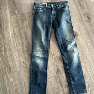 Blå Replay jeans - Säljer ett par klassiska blå Replay jeans med snyggt slitna detaljer och raka ben. Jeansen har fem fickor, kontrastsömmar och Replay-logga på bakfickan. Perfekt för dig som gillar en tidlös och avslappnad look. Kan gå ner i pris 