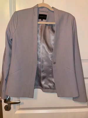Ljusgrå kavaj från Stockholm LM - Snygg ljusgrå kavaj från Stockholm LM med klassisk rak passform och ett stilrent, minimalistiskt snitt. Kavajen har ett silkeslent foder, diskreta fickor och en enkel knapp framtill. Perfekt för dig som gillar en clean och modern look. Aldrig använd pga att det var fläckar (se bilder) när jag kom hem med den så kemtvätt behövs eller om man är duktig på fläckar