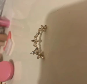 Silvrigt örhänge med pärlor och blommor - Säljer ett snyggt silvrigt örhänge dekorerat med små vita pärlor och glittrande stenar i blommig design. Örhänget har en bågformad stil och detaljer som ger en elegant och trendig look. Ny