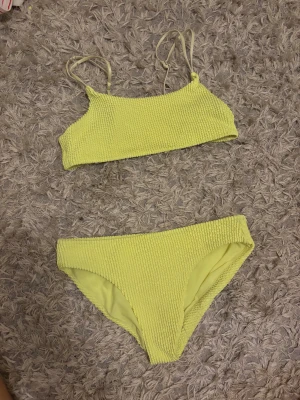 Gul bikini från H&M med ribbad yta - Superfräsch gul bikini från H&M i storlek 134/140. Både överdel och underdel har en ribbad struktur och smala axelband