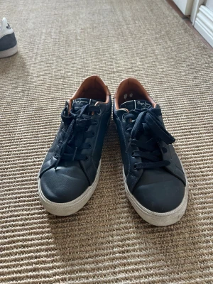 Mörkblå sneakers från Pepe Jeans strl 37 - Mörkblå sneakers från Pepe Jeans med klassisk design, vita sulor och mörkblå snören. Insidan är fodrad i brunt syntetmaterial för extra komfort. Rund tå och platt sula gör dem perfekta för en avslappnad stil. Märkeslogga på plös och sula. Använda max fem gånger. 