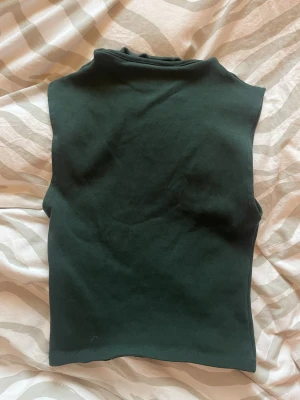 Mörkgrön polotopp från Zara - Säljer en mörkgrön polotopp från Zara i storlek M men känns som S/XS. Toppen är ärmlös och har en hög krage som ger en clean och stilren look. Materialet är mjukt och stretchigt, perfekt att styla med jeans eller kjol.