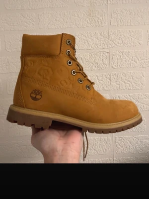 Timberland boots i mocka, strl 38 - Klassiska Timberland boots i ljusbrun mocka med rund tå och grov sula. Skorna har snörning med metallöljetter och den ikoniska Timberland-loggan på sidan. Perfekta för höst och vinter, tillverkade i slitstarkt skinn.