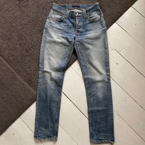 Ljusblåa Nudie Grim Tim Jeans - Riktigt snygga Nudie Jeans med en fet tvätt. | W30 L32. | Riktigt fint skick, finns några fabriksgjorda slitningar. | Längd: 104cm, Midja: 37.5-42cm (Stretch). Pris ej hugget i sten, skriv vid minsta fundering.
