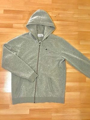 Original Penguin grå zip hoodie – L/M - Grå zip hoodie från Original Penguin i storlek L/G. Klassisk och stilren modell med dragkedja, huva med snörning och den ikoniska lilla pingvin-loggan broderad på bröstet. Mjuk och skön insida, perfekt för vardagsbruk. Den passar på som M.
