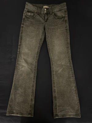 Ljusgrå lågmidjade bootcut jeans från Gina Tricot - Lågmidjade bootcut jeans från Gina Tricot i ljusgrå. Klassisk femficksmodell med dubbla silverknappar i midjan och raka sömmar. Jeansen har en snygg bootcut passform och är tillverkade i mjukt jeanstyg. Lite slitna i bensluten (se bild 3) men annars bra skick. Storlek 158, säljer eftersom de har blivit för små💞