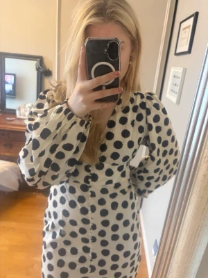 Prickig kortklänning från NEXT - Säljer en vit kortklänning från NEXT med stora svarta prickar och v-ringad hals. Klänningen har långa puffärmar och knappar framtill. Materialet är bomull, vilket gör den skön och lätt att bära. Perfekt för dig som gillar statement-mönster och vill sticka ut. Klänningar är använd endast en gång