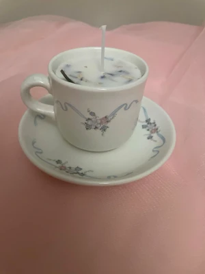 Doftljus av vaniljdoft i en vit tekopp med blommor och blåa streck nr 7 - Det här ljuset är gjort av återanvändbara material. Tekoppen är köpt secondhand och stearinet är från kyrkor som tänkte slänga det. Det här ljuset har en svag doft utav vanilj, så känsliga även kan använda det. Det här ljuset har även torkade blommor på som dekoration. Det finns fler av denna design på hemsidan om man vill köpa sets. 