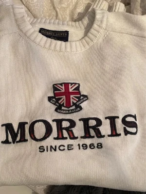Vit stickad tröja från Morris - Säljer en vit stickad tröja från Morris med broderad Union Jack och texten 'MORRIS SINCE 1968' på bröstet. Tröjan har rund halsringning och ribbade muddar. Perfekt för dig som gillar klassisk och stilren design.