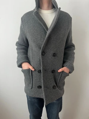 Grå stickad rock från Falconeri  - Säljer en grå stickad rock med dubbelknäppning och stora fickor framtill. Jackan har en hög krage och ribbad struktur som ger en cool och avslappnad look. Perfekt för dig som vill ha något både snyggt och bekvämt till höst och vinter.