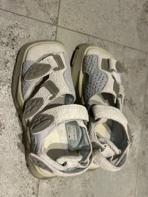 Eytys sandaler i mocka och skinn, strl 41 - Chunky sandaler från Eytys i ljusgrått och beige med ovandel i mocka och skinn. Snygga detaljer med breda remmar och justerbara spännen. Grov sula i TPR för extra komfort och cool look. Perfekta för dig som gillar streetstyle och vill sticka ut. Använt 1 gång endast