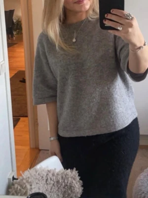 Grå stickad tröja med halvärm - Mysig grå stickad tröja med halvärm och rund hals. Tröjan har en loose passform och är tillverkad i ett mjukt material som känns skönt mot huden. Den har en liten fläck(sista bild) syns knappt!