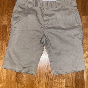 Beiga Dickies shorts  - Snygga beige shorts från Dickies i slim fit-modell. Klassisk design med bälteshällor, två fickor bak med knapp och diskret Dickies-logga ovanför ena bakfickan. Materialet är slitstark polyester som ger en clean och stilren look.