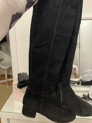 Svarta höga mockastövlar med klack - Säljer ett par svarta höga stövlar i mjuk mocka. De har en låg klack och dragkedja på insidan för enkel påtagning. Stövlarna har en stilren design med rund tå och passar perfekt till både jeans och kjol.