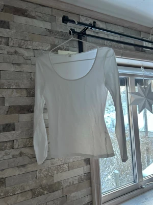 Vit långärmad topp med rund hals - En basic vit långärmad topp med rund halsringning. Enkel och stilren design i mjukt material, perfekt att matcha med jeans eller kjol. Passformen är normal och toppen är tunn och smidig.