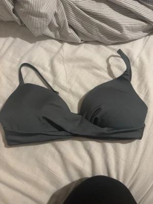 Bikiniöverdel  - Säljer en snygg mörkgrön bikiniöverdel från H&M i storlek 75B då den blivit för liten. Modellen har vadderade kupor och justerbara axelband med guldfärgade detaljer. Materialet är mjukt och syntetiskt, perfekt för strand eller pool.