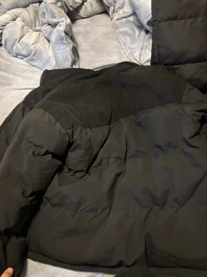 Svart pufferjacka från The North Face - Säljer en svart pufferjacka från The North Face med coolt manchestertyg på axlar och krage. Jackan har dragkedja framtill, höga fickor och en schysst logga på bröstet. Perfekt för kalla dagar och riktigt snygg stil.