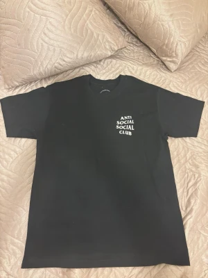 Svart Anti Social Social Club t-shirt - Svart t-shirt från Anti Social Social Club med vit logga på bröstet och stor logga på ryggen dekorerad med rosa blommor och fjärilar. Klassisk passform och tillverkad i mjuk bomull. Perfekt för dig som gillar streetwear och vill sticka ut.