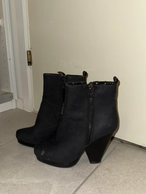 Svarta boots med klack och dragkedja - Säljer ett par svarta boots med hög klack och dragkedja på sidan. Skorna har en något spetsig tå och är tillverkade i mockaimitation. Perfekta för dig som vill ha en edgy look till hösten eller vintern.
