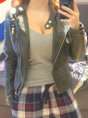 Svart skinnjacka med detaljer - Säljer en svart skinnjacka med coola quiltade detaljer på ärmarna och dragkedjor framtill. Jackan har bälte i midjan och en snygg krage med tryckknappar. Perfekt för dig som vill ha en edgy look.