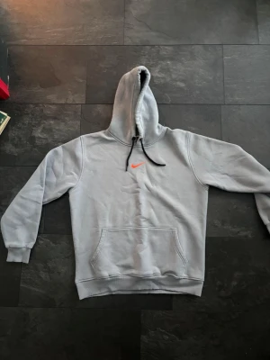 Grå nike hoodie Strl M/L - Tja, jag säljer en grå nike hoodie i perfekt skick. Den har en orange logga på bröstet och svarta snören. Inga defekter. Den är i storlek L men jag upplever att den passar M också. Kontakta gärna vid frågor och funderingar.