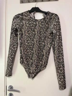 Leopardmönstrad långärmad body-topp  - Säljer en snygg långärmad body från XOXO b.friends i leopardmönster. Toppen är beige med svarta fläckar, har rund hals och en liten knappdetalj i nacken. Materialet är mjukt och stretchigt, perfekt för dig som vill sticka ut. Storlek 170 men skulle säga den passar S eller M. Använd fåtal gånger. Pris kan alltid diskuteras!🤗