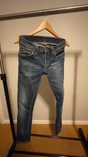 Blå jeans från Nudie - Snygga blå jeans från Nudie Jeans Co i klassisk femficksmodell. Jeansen har en lätt tvättad look med kontrastsömmar och läderpatch bak. Modellen är rak och passar perfekt till en avslappnad stil. Tillverkade i slitstarkt jeanstyg av bomull.
