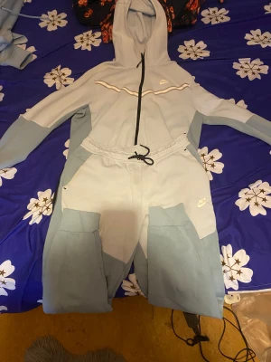 Ljusblå Nike dress  - Nike dress i ljusblå och grå toner med hel dragkedja och huva. Snyggt broderad Nike-logga på bröstet, ribbade muddar och paneler i olika färgblock. Perfekt för chill eller träning, riktigt skön och stilren design.