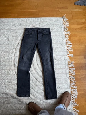 Svarta Nudie Jeans grimTim 29/32 - Säljer ett par svarta jeans från Nudie Jeans i storlek 29/32. Jeansen har klassisk femficksdesign, svarta sömmar och en slim passform som sitter snyggt längs benen. Perfekta för dig som gillar en clean och stilren look.