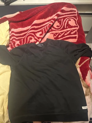 Svart sweatshirt med rund hals - En stilren svart sweatshirt med rund hals och långa ärmar. Tröjan har en enkel design utan mönster, med synliga sömmar vid axlarna och en liten vit etikett vid nederkanten. Perfekt för chill dagar och enkel att matcha med jeans eller joggers.