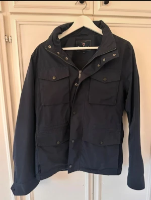 Mörkblå field jacket från Bondelid - Snygg mörkblå vindjacka från Bondelid. Materialet är slitstark polyester och passformen är normal. Modellen är 172cm och 65kg. Priset är diskuterbart!