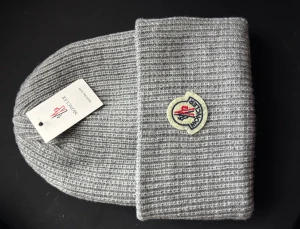 Grå ribbad Moncler mössa - Snygg grå ribbstickad mössa från Moncler med klassisk logopatch framtill. Mössan har bred uppvikt kant och är tillverkad i mjuk ull som håller dig varm. Perfekt för dig som vill ha en clean och stilren look med exklusiv känsla.