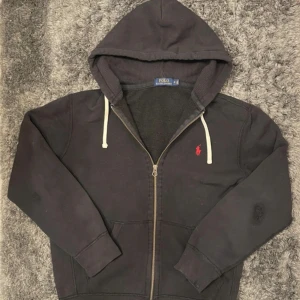 Svart hoodie från Polo Ralph Lauren - Hej, säljer en riktigt fin svart Ralph Lauren Hoodie med en röd pony. Hoodien har ett par slitningar, se skick enligt bilder. Utöver detta är den riktigt fin. Den är i storlek M. Hör av er vid frågor!