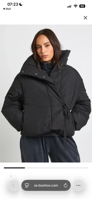 Svart pufferjacka med knyt från Boohoo - HELT NY MED LAPPEN KVAR!! Svart pufferjacka med hög krage och omlottstängning med knyt i sidan. Jackan har en oversized passform och är tillverkad i ett syntetmaterial som håller dig varm. Perfekt för dig som gillar en chill och trendig look.