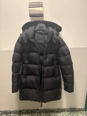 Cedrico Lorin dunjacka storlek M/L - Svart dunjacka från Cedrico med huva och fluffig kant, långa ärmar och flera dragkedjeförsedda fickor. Jackan är figur sydd passform som håller dig varm hela vintern. Perfekt för dig som vill ha en stilren och praktisk vinterjacka. Dock mer som en M Än L  Päls på luvan nypris 8900kr 