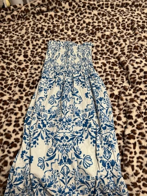 Lång kjol från H&M - Supersöt blåvit kjol från H&M med smock upptill och ett vackert blommigt mönster. Köpt på plick och använts en gång. Har en luftig passform, perfekt för varma dagar. Tillverkad i mjuk bomull som känns skön mot huden.