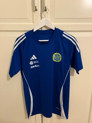 Blå GIF Sundsvall fotbollströja Adidas - Säljer en blå GIF Sundsvall fotbollströja från Adidas med vita detaljer och tryck. Tröjan har korta ärmar, klubbmärke på bröstet, sponsorer som SCA, Stadium och McDonald's logga på ryggen. Tillverkad i lätt och ventilerande polyester.