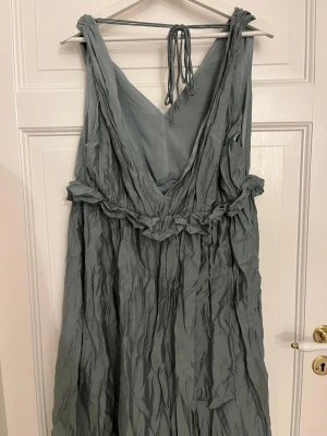 Ljusgrön turkos långklänning - Säljer en flowy ljusgrön turkos långklänning från H&M med v-ringad hals och knytband i nacken. Klänningen har ett snyggt rynkat tyg och ett band i midjan som ger en cool boho-vibe. Perfekt för dig som gillar avslappnad och trendig stil.