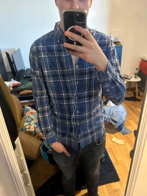 Ralph Lauren skjorta  - Snygg blårutig skjorta från Ralph Lauren med klassisk button-down krage och broderad logga på bröstet. Skjortan har långa ärmar, vita knappar och är gjord i mjuk bomull. Perfekt för dig som gillar en stilren och tidlös look.