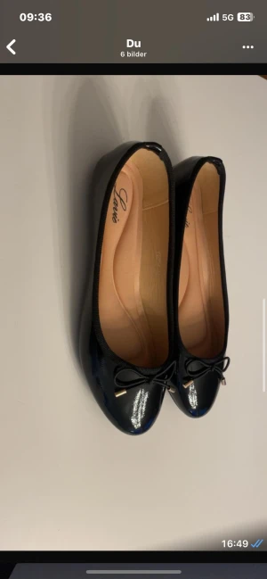 Svarta ballerinaskor med rosett från Lululia - Snygga svarta ballerinaskor från Lululia med glansig finish och rund tå. Dekorerade med en liten rosett framtill med metalländar. Skorna har en platt sula och mjuk innersula i beige ton. Perfekta för dig som gillar klassisk och stilren look. Helt nya aldrig använda.