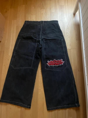 Svarta baggy jeans med graffiti loga som det står wexwear på! - Säljer ett par svarta jeans med breda ben och kontrastsömmar. De har stora fickor både fram och bak, och en fet röd graffiti patch på ena bakfickan som ger street vibe. Materialet är jeans och modellen är loose fit med hög midja.
