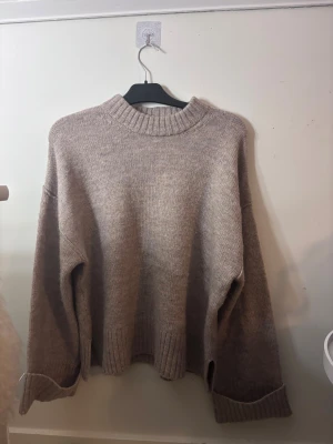 Beige stickad tröja från Gina Tricot - Supermysig beige stickad tröja från Gina Tricot med breda ribbade muddar och uppvikta ärmslut. Tröjan är i storlek M. Använd fåtal gånger så inga defekter