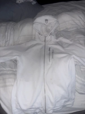 Vit hoodiejacka från Sail Racing - Säljer en vit hoodiejacka från Sail Racing med dragkedja framtill och en extra ficka med zip på bröstet. Jackan har huva med snörning och är perfekt för chill dagar. Stilren design med logga på bröstet.