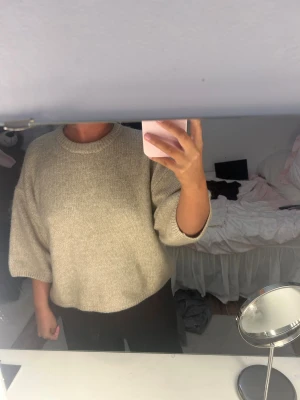 Beige stickad tröja från Gina Tricot - Mysig beige stickad tröja från Gina Tricot med rund hals och ribbade detaljer vid halsringning, ärmslut och nederkant. Tröjan har en loose passform och lite kortare ärmar som ger en chill vibe. Perfekt att slänga på sig när det är kallt ute.