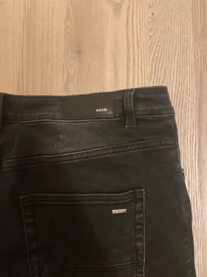 Svarta jeans från Amiri - Snygga svarta jeans från Amiri med klassisk femficksdesign och diskret logga på bakfickan. Jeansen är tillverkade i 100% bomull med ribbade detaljer i bomull och kashmir för extra komfort. Passformen är rak och stilren, perfekt för en modern look.