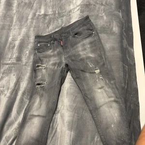 Grå skinny jeans från Dsquared2 - Snygga grå jeans från Dsquared2 med slitna detaljer och trasiga partier på framsidan. Modellen är slim fit med klassisk femficksdesign och coola färgstänk. Märkespatch bak och röd Dsquared2-tag vid fickan. Perfekt för dig som gillar streetstyle.