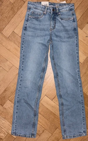 Blå raka barnjeans från LAB Industries - Snygga ljusblå jeans från LAB Industries med klassisk femficksdesign och raka ben. Jeansen har normal passform, midwaist och är tillverkade i mjukt bomullsmaterial. Perfekt för dig som gillar en enkel och clean look. 
