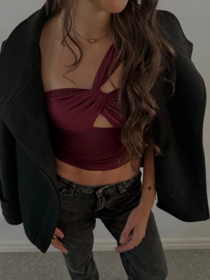 Snygg festtopp  - Säljer en vinröd topp med omlott-design och snygg twist framtill. Toppen har one shoulder och materialet är mjukt och stretchigt, perfekt för att styla med jeans eller kjol.