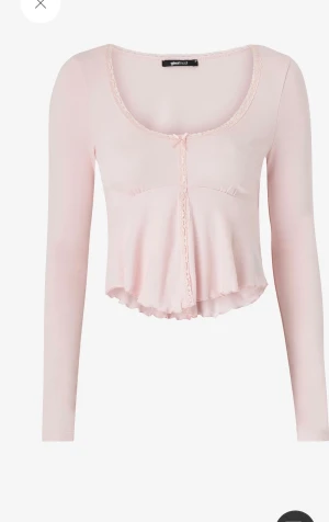 Ljusrosa långärmad topp från Gina Tricot - Supersöt ljusrosa topp från Gina Tricot med lång ärm och croppad passform. Rundad halsringning med spetskant och liten rosett framtill. Mjuk och stretchig i materialet, med volangdetalj nedtill och dekorativ spets längs mitten.